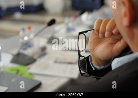 A mature man wearing glasses stands in a corporate meeting room, looking out with a contemplative expression Stock Photo
