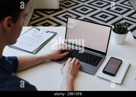 Closeup of unrecognizable man using laptop with white screen mockup on desk in office, hands typing Stock Photo