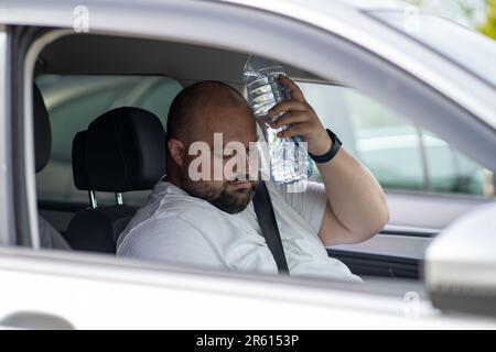 Weary overweight man drives car with broken air conditioner in hot summer weather. Stock Photo