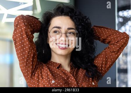 Happy and smiling successful hispanic business woman finished work satisfied with work result and achievement, hands behind head and smiling close up. Stock Photo
