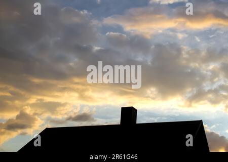 Defocus steel roof on sunset sky background. Dark rain clouds above the modern roof. Roof with new black roofing tiles double flap on residential Stock Photo