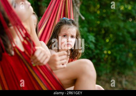 Three young female friends enjoying a sunny day in a backyard, relaxing and hanging out together on a colorful hammock Stock Photo