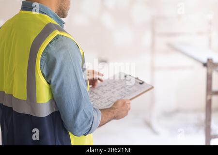 Foreman in vest checking drawing plan of big house holding clipboard in hands Stock Photo