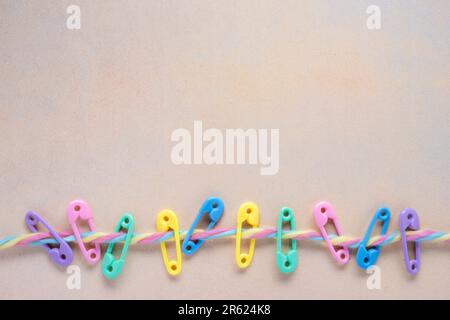 colorful baby concept flat lay with bright plastic diaper pins on a multi colored fuzzy yarn line with mottled yellow background Stock Photo
