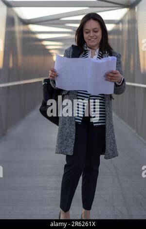 A female adult is crossing a bridge while looking at a document in her hand Stock Photo
