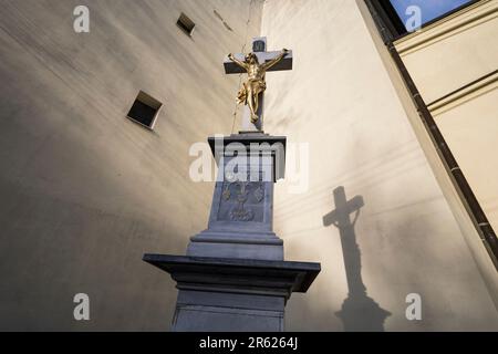 Pedestal with christian cross and crucified Jesus Christ. Christianity and religious symbol. Evening light with shadow on the building of church. Very Stock Photo