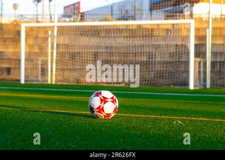 A soccer ball in the classic red and white colors lays on the ground in front of a goalkeeper, ready to be used during a game Stock Photo