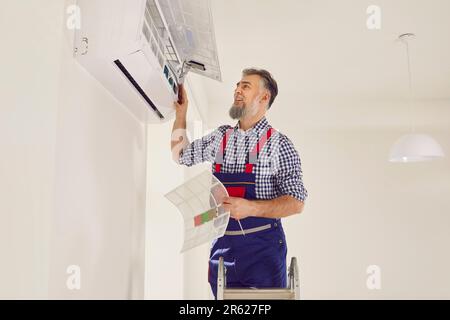 Professional mature electrician man maintaining modern air conditioner indoors changing filter. Stock Photo