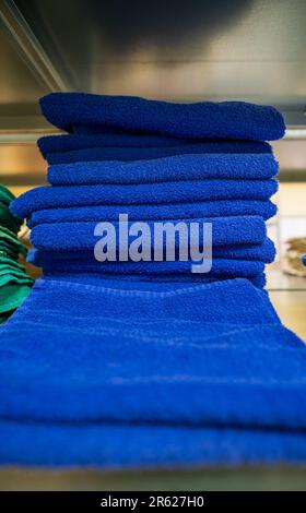 Clean terry soft towels in blue folded, stacked in a pile. Stacks of towels stacked on shelves in the laundry room. Stock Photo