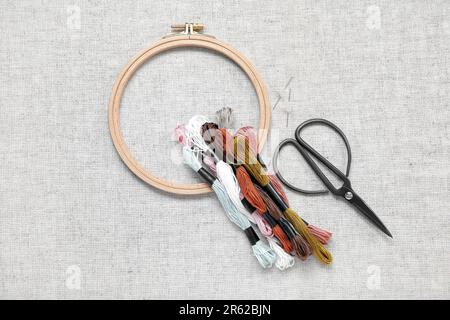 Wooden embroidery hoop with scissors, needles and mouline threads on canvas background Stock Photo