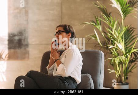 Side view of a middle-aged woman in formal wear sitting indoors and talking on a mobile phone Stock Photo