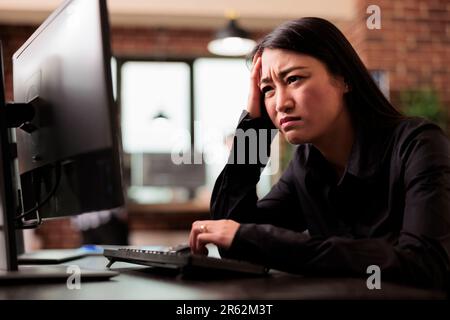 Tired tech engineer was struggling to keep up with the demands of the software development project, feeling the stress of overwork. Coder writing ai algorithm and sitting at desk in it company. Stock Photo
