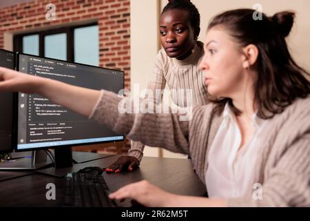Diverse coders working on terminal window with html script, typing server code on computer, sitting at desk in big data room. System engineers programming user interface in it developing agency. Stock Photo