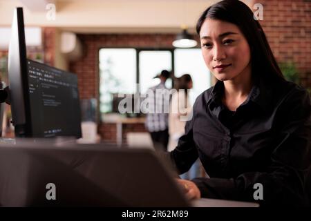 Asian freelance coder analyzing compiling html code on computer display, working on interface development. Programming engineer using terminal window with firewall server data in it big data agency Stock Photo