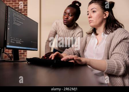 Diverse team of tech enginners talking about programming in it development agency. African american programmer compiling app language with software developer, innovating online server algorithms. Stock Photo