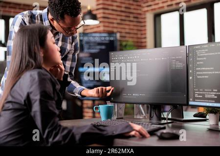 Diverse programmers discussing about html code compiling discovers errors, standing in front of multiple screens in startup office. Software developers working on server interface development. Stock Photo
