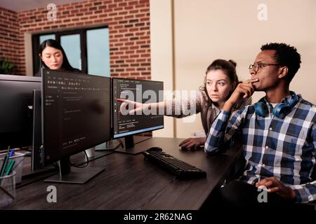 Software developer asking coder for help with html code, pointing at database script on terminal window. Team of programming engineers working on app developing program in data room. Stock Photo