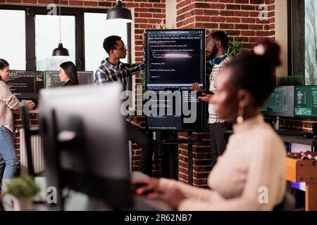 Africann american system engineers analyzing source code looking for errors, checking big tv monitor in it agency office. Software developers working on cyber security innovation in it agency. Stock Photo