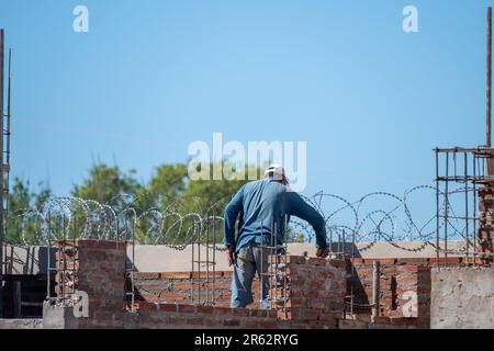 A construction worker wearing a hard hat and safety vest is seen carefully constructing a brick wall with a trowel Stock Photo