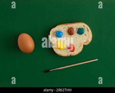 Abstract Easter composition made of egg and slice of bread with colorful palette. Green background. Topy view, flat lay. Stock Photo