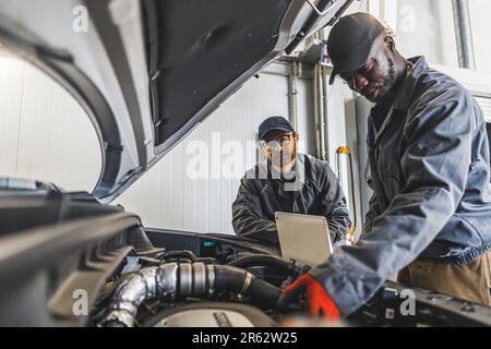 Two men mechanics completing car engine diagnostics with laptop in a repair shop. High quality photo Stock Photo