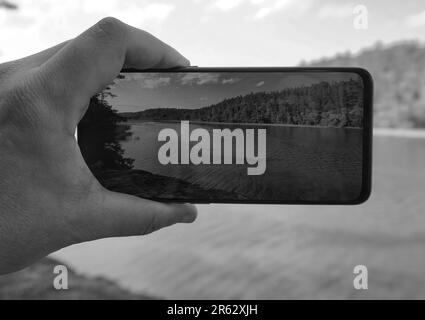 Cropped hand photographing lake through mobile phone Stock Photo