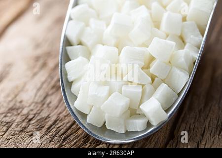 Dried candied cubes of coconut fruit in metal scoop on wooden table (Selective Focus, Focus in the middle of the image) Stock Photo
