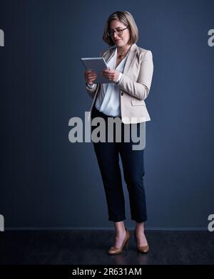 The corporate world is her playground. Studio shot of an attractive young corporate businesswoman using a tablet against a dark background. Stock Photo