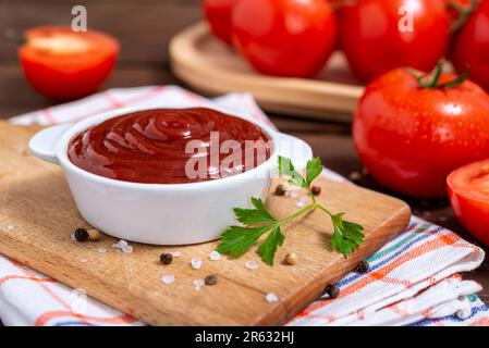 Ceramic bowl of ketchup or tomato sauce, spices and fresh tomatoes on wooden table. Selective focus. Stock Photo