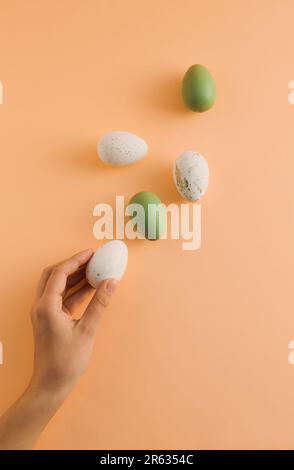 Easter pattern made of white and green eggs and woman's hand on pastel orange background. Minimal Easter holiday composition. Creative food concept. T Stock Photo