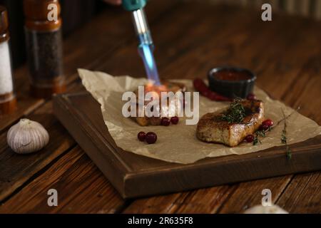 Cooking meat medallions with manual gas burner on wooden table in photo studio. Food stylist Stock Photo