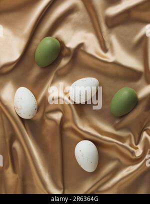 Easter eggs on golden silk background. Luxury texture idea. Minimal Easter holiday composition. Top view, flat lay. Stock Photo