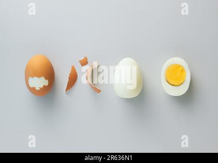 Whole chicken egg, egg without eggshell and cracked half in the middle with yolk on grey background. Minimal healthy food concept. Top view, flat lay. Stock Photo