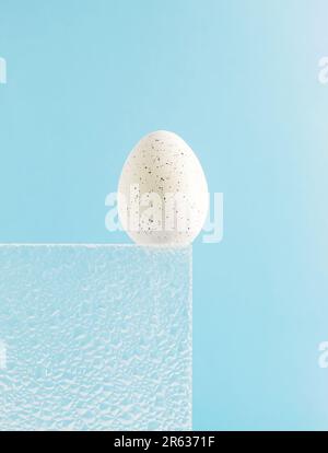 Trendy composition made of white Easter egg on sky blue background. Embossed glass texture background. Minimal festive concept. Abstract Easter card. Stock Photo