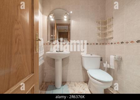 Conventional unfurnished bathroom with arched mirror, white porcelain sanitary ware and oak door Stock Photo