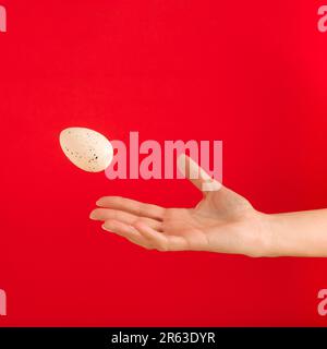 Woman's hand throwing away white egg on red background. Minimal Easter concept. Copy space. Stock Photo