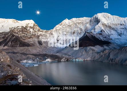 Gray moraine lake and snowy mountain peak in the moonlight in Himalayas, Nepal. Mirror water of a big moraine lake. Stock Photo