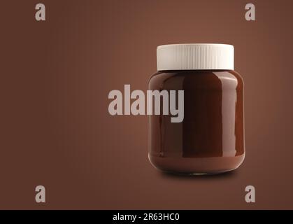 Chocolate spread or nougat cream with hazelnuts in glass jar on a brown background with space for text Stock Photo