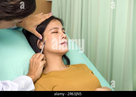 Doctor giving female patient medical injection in temporal. Atmosphere at cosmetic surgery department in hospital clinic. Stock Photo