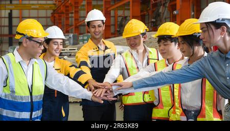 Group of male and female factory labor join hands together after finish meeting. Everyone wearing safety uniform and helmet. Workers working in the me Stock Photo