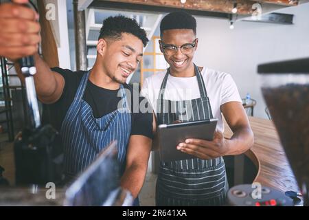 Table number five needs two cappuccinos. two young men using a digital tablet while making coffee at a cafe. Stock Photo