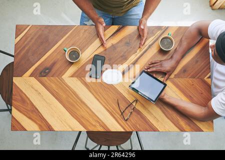 Strategy and coffee go hand-in-hand. High angle shot of two unrecognizable friends sitting together and using a tablet in a coffeeshop. Stock Photo