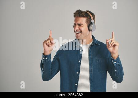 Rocking out to some cool tunes. Studio shot of a young man listening to music against a grey background. Stock Photo