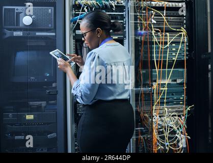 Server room, woman and engineer with tablet for cybersecurity, programming or cable maintenance. Black female technician in datacenter for network Stock Photo