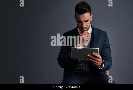 Getting it done digitally. Studio shot of a stylish young businessman using a digital tablet against a gray background. Stock Photo