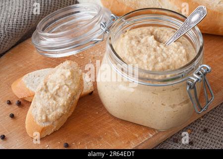 Fresh homemade mushroom pate in a jar and on a baguette slice on a rustic background, with champignons. Stock Photo