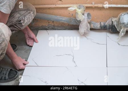 A male builder tiler lays floor ceramic tiles. Selective soft focus Stock Photo