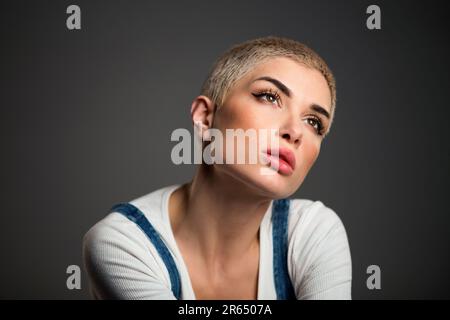 Thoughtful young stylish female model with short blond hair un casual clothes looking away dreamily against black background Stock Photo