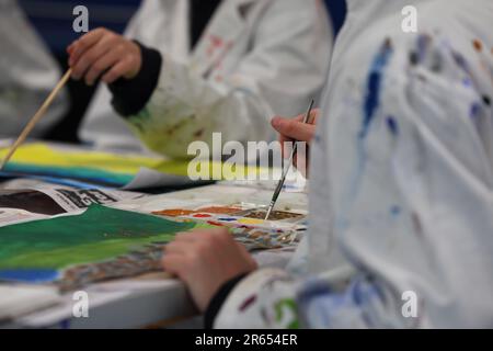 Visual art students wearing stained white smocks or aprons mixing paints on a paint palette for a artwork or painting project. Art education in a shoo Stock Photo