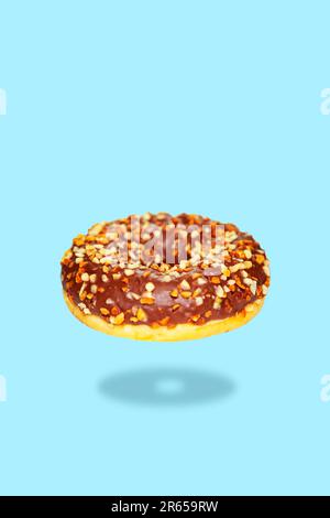 Flying donut with chocolate icing and nuts isolated on a blue background. Stock Photo